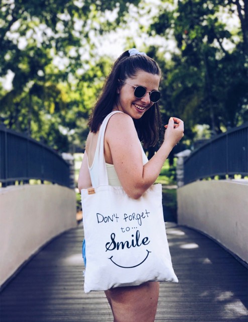 Tove wearing a summery outfit, sunglasses, and a canvas bag saying: Don't forget to smile!
