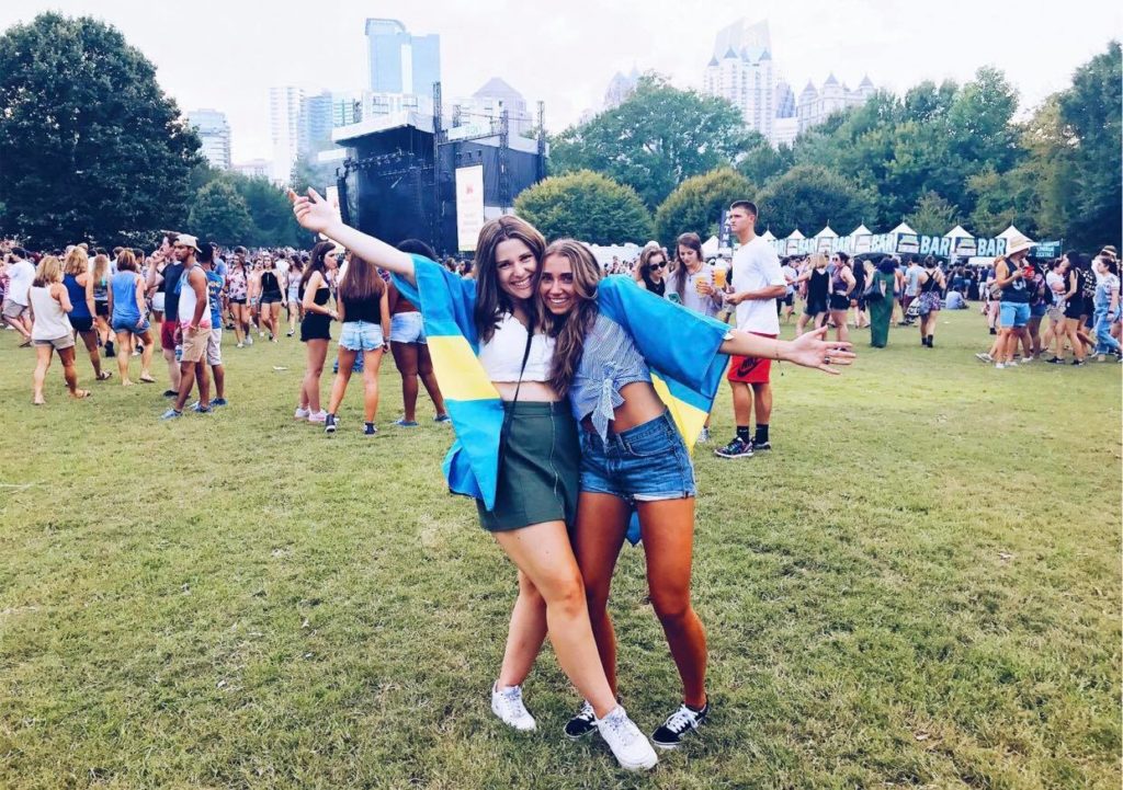 Tove and her friend, both wearing a Swedish flag over their shoulders, at a festival.