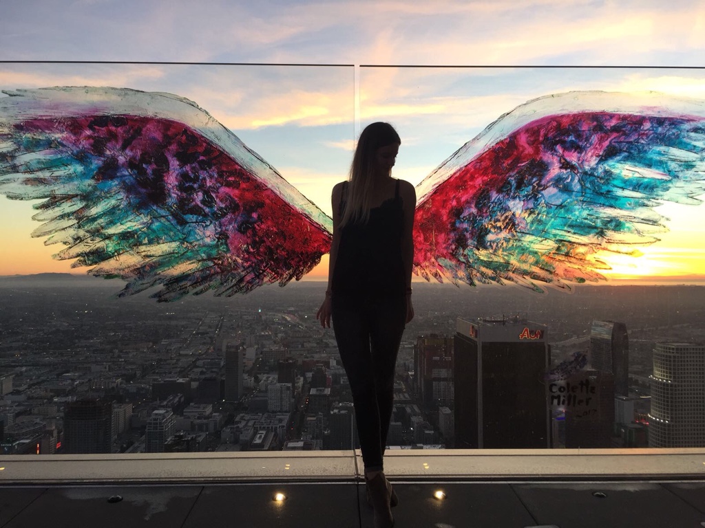 Vanessa standing on OUE Skydeck, in front of some painted on angel wings.