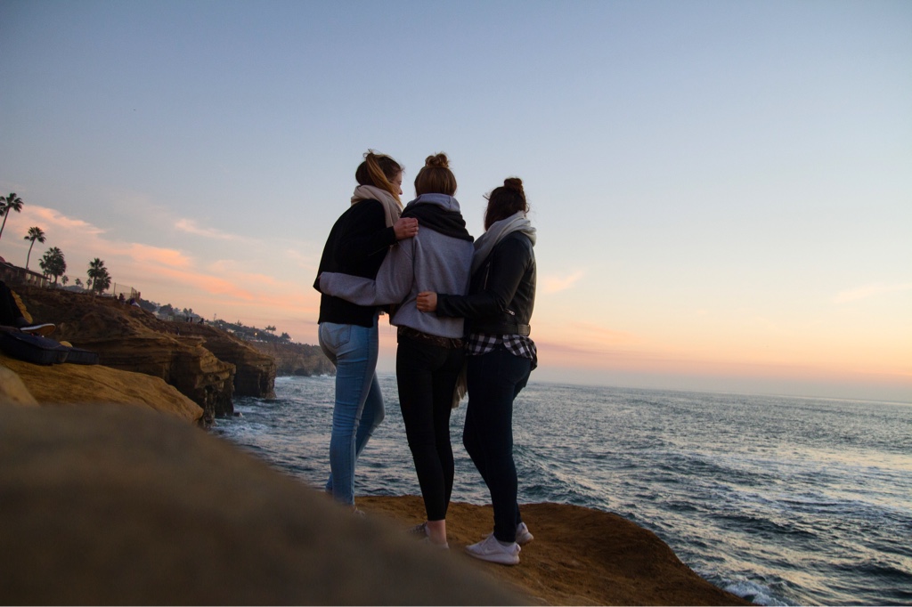 Vanessa and her two friends standing on a rock by the beach, overlooking the ocean.