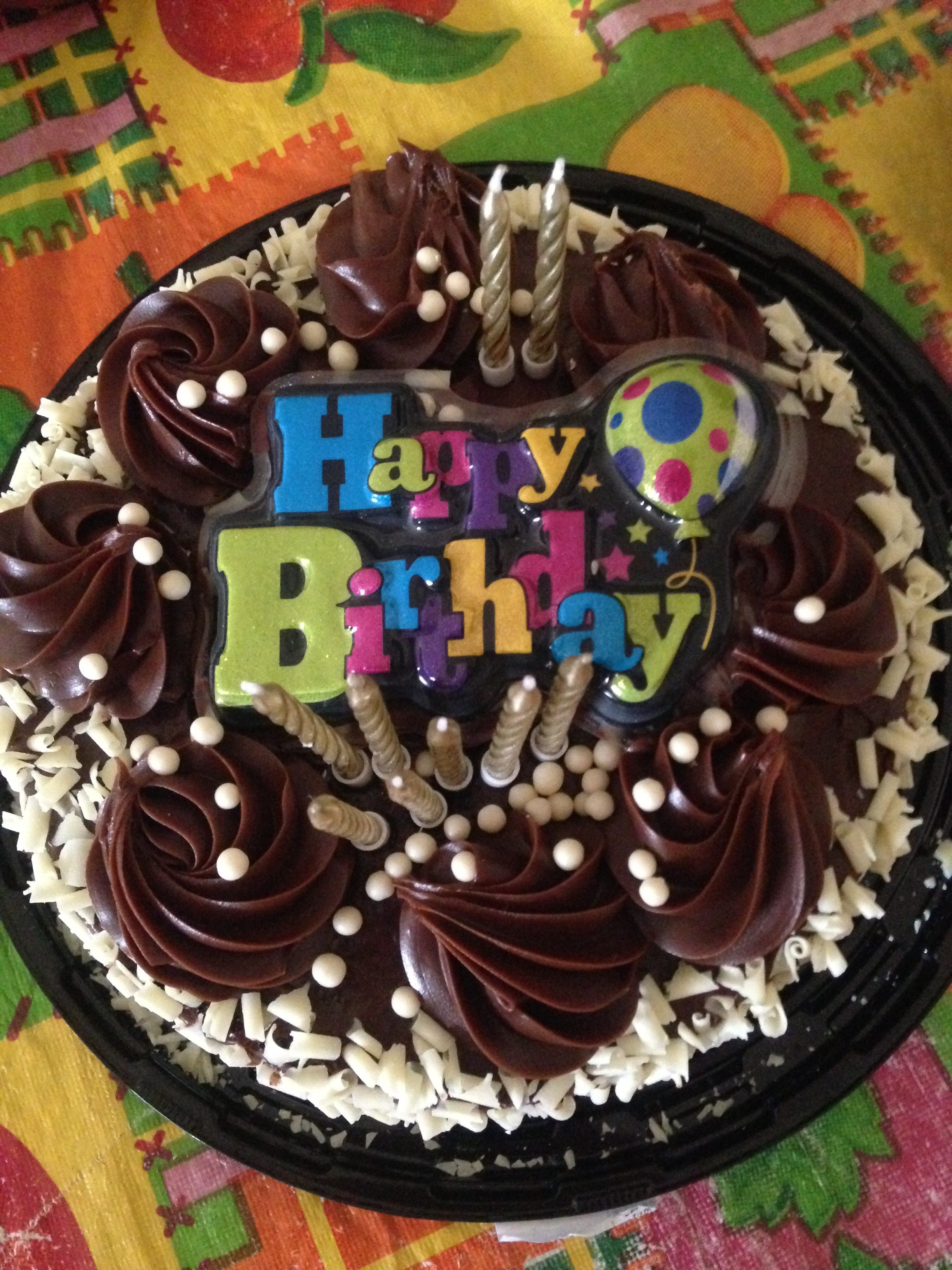 A chocolate birthday cake with Happy Birthday writing and sprinkles on top.