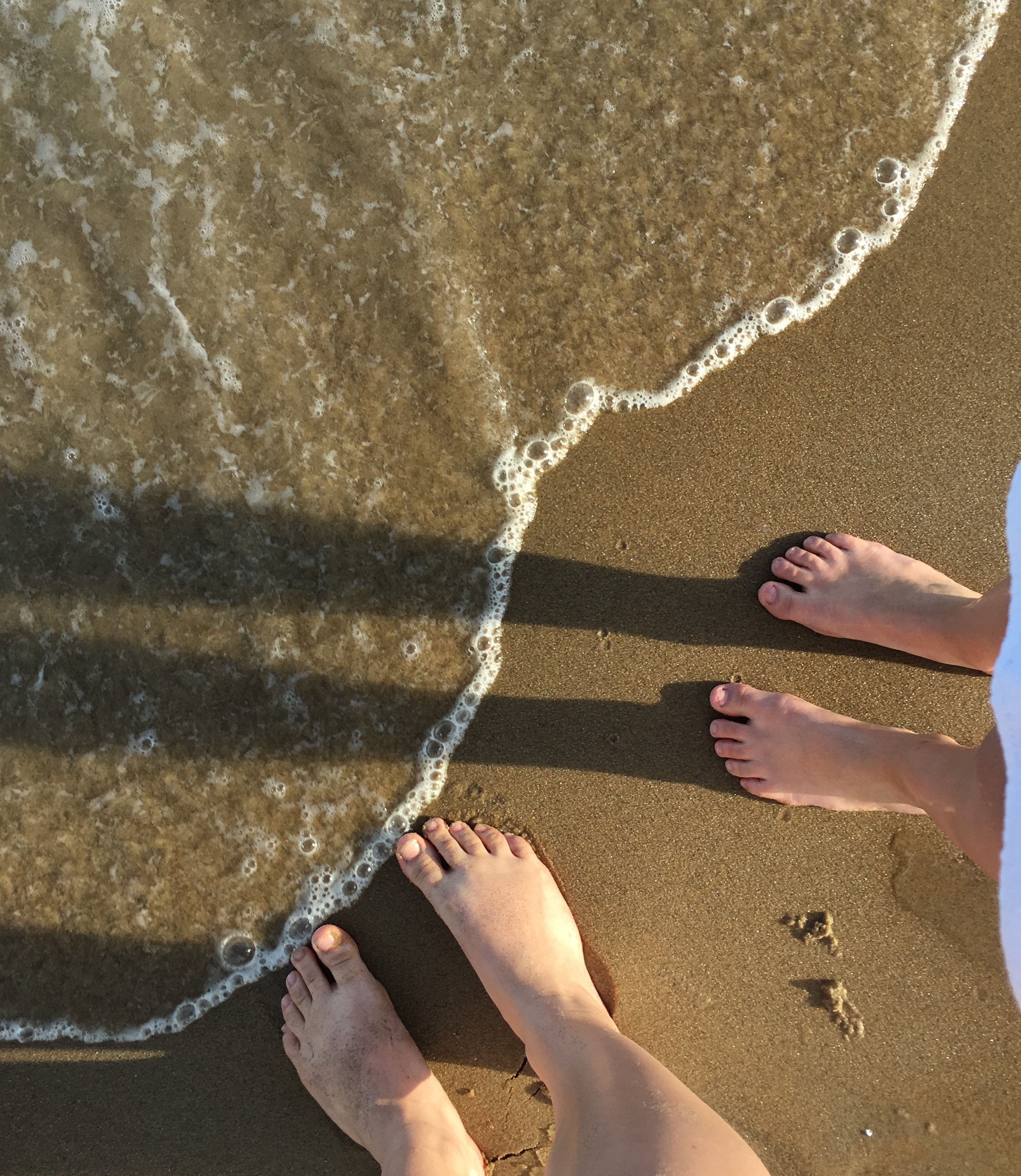 Two pairs of feet on the beach, just about to touch the water.