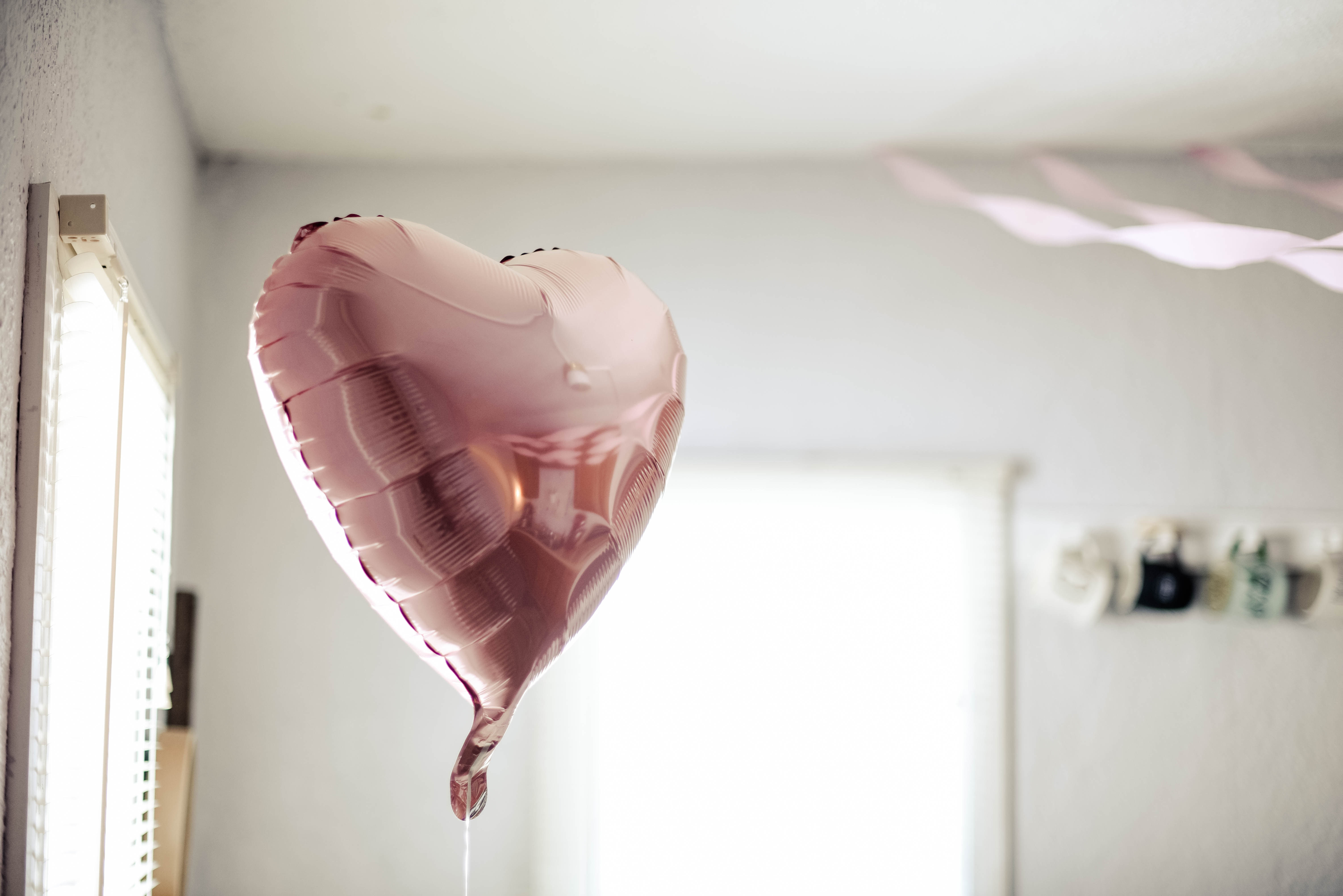A pink, heart-shaped balloon in the middle of a bright room.