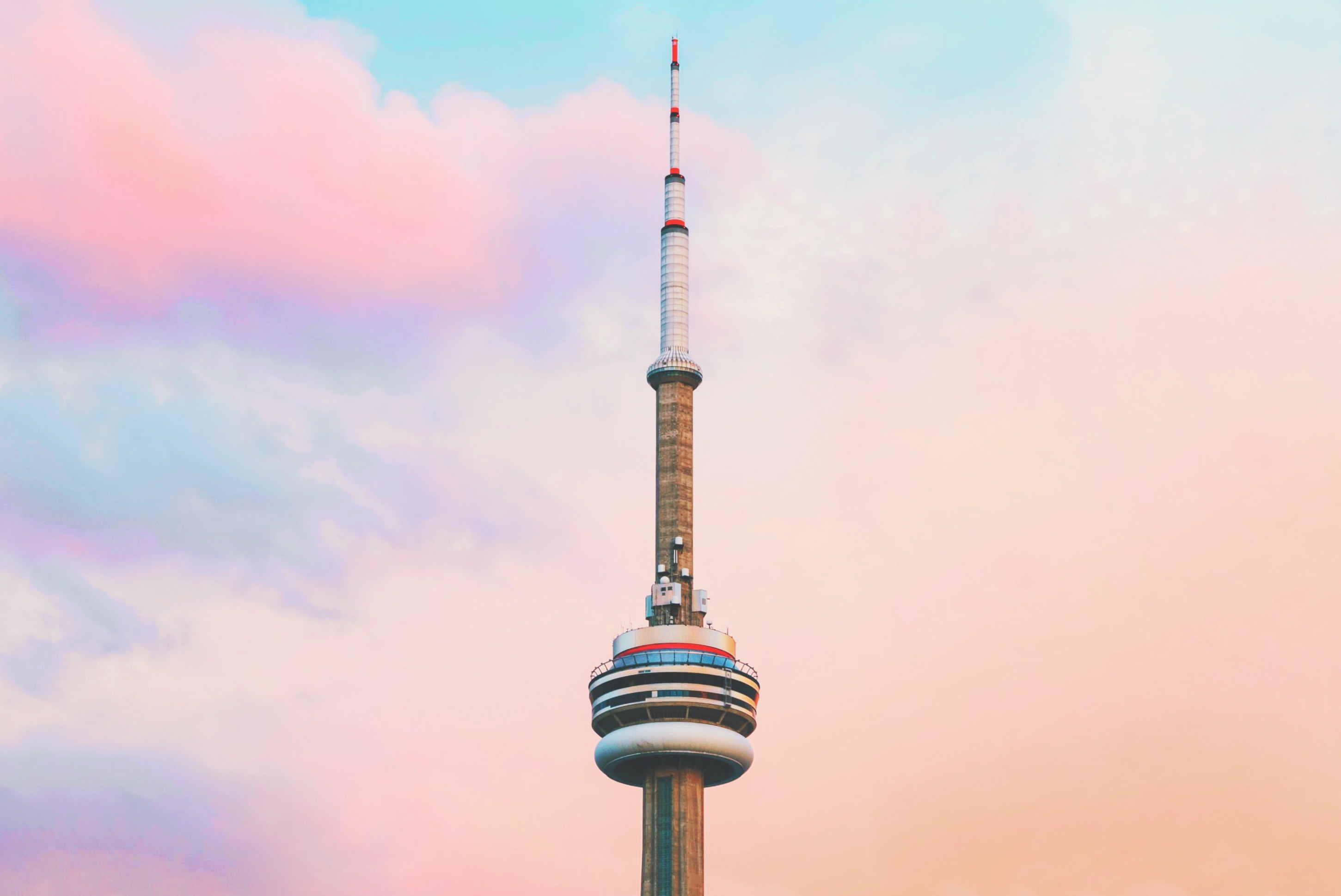 The top of the iconic CN Tower, surrounded by a blue sky and pink clouds.