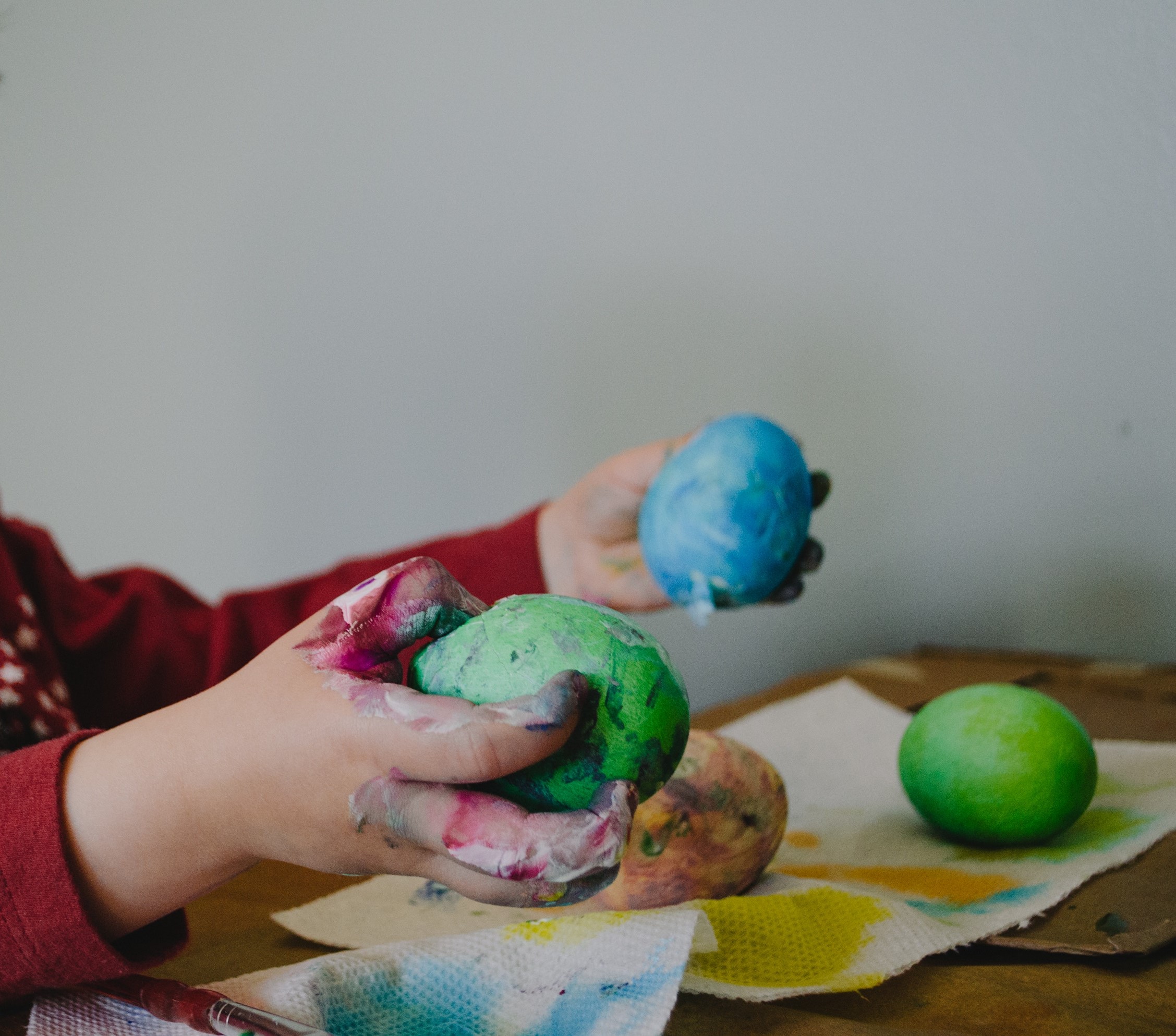 A kid holding two colored Easter eggs in its paint-covered hands.